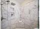 Close up of a marble shower featuring shower head, built in shelving, and a corner seat at 1630 Reindeer Rdg, Alpharetta, GA 30005