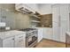 Gas range with stainless hood and modern cabinets, accented by a trendy backsplash and floating shelves at 140 Rolison Way, Fayetteville, GA 30214