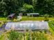 This aerial shot features a greenhouse, shed, and farmland nestled among lush greenery and mature trees at 220 Gamble Dr, Carrollton, GA 30116