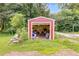 The outdoor shed has red siding, a white trim, open garage door, and is surrounded by green grass and trees at 220 Gamble Dr, Carrollton, GA 30116