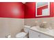Bright half-bathroom featuring a red accent wall, tiled wainscoting, mirror, toilet, sink, and neutral colored countertops at 425 Houze Way, Roswell, GA 30076