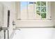 Close-up of a soaking tub with a sleek handheld shower fixture and a bright, window view at 560 Edgehill Pl, Johns Creek, GA 30022