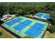 Aerial view of blue and green tennis courts surrounded by lush trees offering a recreational amenity at 5347 Harbury Cv, Suwanee, GA 30024
