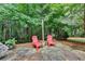 Secluded stone patio featuring two red Adirondack chairs surrounded by lush greenery and mature trees at 6520 Fairfield Trce, Suwanee, GA 30024
