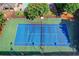 Aerial view of a blue and green tennis court surrounded by trees and fencing, perfect for recreational play at 6520 Fairfield Trce, Suwanee, GA 30024