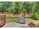 Backyard patio area with built in grill and manicured landscaping and wooded backdrop at 2748 Hidden Falls Dr, Buford, GA 30519