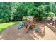 View of a wooden playground with a slide and swings set in a mulch area, surrounded by trees at 360 Hannaford Dr, Roswell, GA 30075