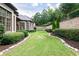 Lush backyard with manicured lawn, decorative stone borders, mature shrubbery, and a brick retaining wall at 9695 Almaviva Dr, Alpharetta, GA 30022