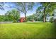 Expansive backyard with lush green grass and mature trees, featuring a red barn and a swimming pool in the distance at 205 Cobb St, Palmetto, GA 30268