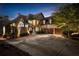 An evening shot of the home's exterior with landscape lighting showcasing the three-car garage and paved driveway at 1525 Lockridge Dr, Cumming, GA 30041