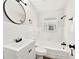 Bathroom featuring a tub, round mirror, white subway tile, white sink, and black fixtures at 5619 Beaver Sw Dr, Mableton, GA 30126