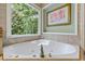Soaking tub beside a large window and rose art in a neutral, decorated bathroom at 1788 River Bluff Vw, Duluth, GA 30097