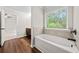 Bathroom showcasing a white bathtub with tile surround and a view of the backyard through a window at 3865 Rifflepool Ct, Douglasville, GA 30135