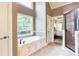 Bright bathroom showcasing a soaking tub with window, tiled floors, and walk-in shower with glass door at 240 Chandler Walk, Loganville, GA 30052