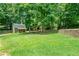 Large grassy backyard with a storage building, wooden deck, and a retaining wall surrounded by mature trees at 3372 English Oaks Nw Dr, Kennesaw, GA 30144