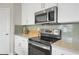 Close-up view of stainless steel oven and microwave with grey subway tile backsplash and modern white cabinets at 2820 Aralynn Way, Atlanta, GA 30337