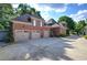 Three-car garage with brick exterior and concrete driveway, surrounded by lush trees and blue skies at 2160 Kensington Gates Nw Dr, Kennesaw, GA 30152