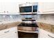 Stainless steel stove and microwave with granite countertops and white marble backsplash at 1200 Martins Chapel Se Ln, Lawrenceville, GA 30045
