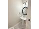 Charming powder room with a pedestal sink, round mirror, and classic black and white tile flooring at 3871 Portland Trail Dr, Suwanee, GA 30024