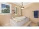 Relaxing bathtub with tile surround, a modern light fixture, and natural light from windows at 7575 Hunters Woods W Dr, Atlanta, GA 30350