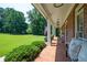 Charming covered front porch with classic brick flooring and inviting bench seating with a green front lawn at 1642 Reflections Trl, Powder Springs, GA 30127