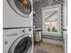 Modern laundry room with stacked washer/dryer, patterned wallpaper, and natural light from the window at 3952 Dragon Fly Ln, Loganville, GA 30052