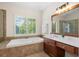 Bright bathroom features a soaking tub under a window, a glass shower, and a vanity with wood cabinets and a mirror at 1215 Renaissance Se Ct, Mableton, GA 30126
