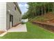 Spacious backyard with a patio, green lawn, wooden retaining wall, and view of the surrounding pine trees at 12148 Flannery Ln, Hampton, GA 30228