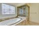 Luxurious bathroom with a jetted tub, travertine tile, glass shower and decorative window at 8230 Royal Melbourne Way, Duluth, GA 30097