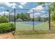 A fenced tennis court with a blue and green surface, surrounded by lush greenery and a building in the background at 3202 Lucky Pl, Conyers, GA 30013