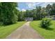 A long driveway leading to a charming two-story home with lush green grass and tall trees in the background at 174 Village Dr, Hiram, GA 30141