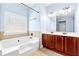 Bright bathroom featuring a tub with tiled surround and a double vanity with dark wood cabinets at 5430 Breckinridge Ln, Cumming, GA 30040