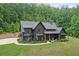 Aerial view of a dark modern farmhouse boasting a three car garage, basketball court, lush lawn and woods at 2100 Mountain Cove Ct, Woodstock, GA 30188