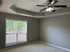 Bedroom featuring a large window, neutral carpet, and tray ceiling with ceiling fan and light fixture at 5415 Windcrest Ln, Suwanee, GA 30024