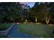 Lush backyard with well-maintained lawn, garden beds, and a gravel pathway, illuminated for evening enjoyment at 2429 Kirk Nw Ln, Kennesaw, GA 30152
