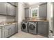 Well-lit laundry room featuring gray cabinets, granite countertops, and modern washer and dryer at 5507 Aviemore Ct, Suwanee, GA 30024