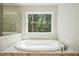 Elegant bathroom featuring a marble-encased soaking tub situated beneath a window with views of mature trees at 5394 Pebblebrook Se Ln, Mableton, GA 30126