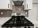 Close up of stainless steel gas stovetop and range hood, complemented by white cabinets and a tile backsplash at 975 Memory Ln, Lawrenceville, GA 30044