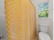A well-lit bathroom featuring a toilet in an alcove with a window and a yellow and white patterned shower curtain at 179 Hunters Crk, Dallas, GA 30157