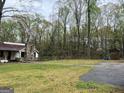 Exterior shot showcasing a ranch-style house with a stone chimney and a wooded area as seen from the lawn at 2497 Old Jackson Rd, Locust Grove, GA 30248