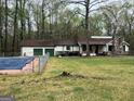 Ranch-style house with stone chimney, green grass, in a wooded setting with a covered swimming pool in the foreground at 2497 Old Jackson Rd, Locust Grove, GA 30248