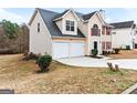 View of the tan home showcasing a two-car garage and landscaped front yard at 2916 Ward Lake Way, Ellenwood, GA 30294