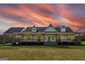 Charming farmhouse with an expansive front porch, pristine white siding, and a lush green lawn at sunset at 271 Trestle Rd, Locust Grove, GA 30248