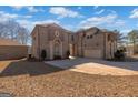Rear exterior view of the brick home with a three-car garage and an ample driveway on a sunny day at 1408 Hemphill Rd, Stockbridge, GA 30281