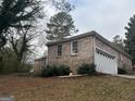 View of brick home with a 2-car garage, surrounded by mature trees at 676 Bralorne Dr, Stone Mountain, GA 30087