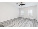 Neutral bedroom with wood-look floors, a ceiling fan, and two windows allowing plenty of natural light at 3050 Azteca Way Ln, Dacula, GA 30019
