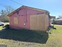 Damaged side of pink ranch home with boarded windows, yellow trim, and green grass at 329 Oak Dr, Social Circle, GA 30025