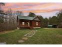 Inviting log cabin with stone path, carport, and lush lawn under a colorful sunset sky at 1266 Martin Mill Rd, Moreland, GA 30259