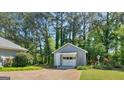 A detached garage with white trim sits in a serene, wooded setting, complemented by colorful flower beds at 230 Acorn Ct, Mcdonough, GA 30253