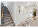 Well-lit hallway with carpeted stairs, stylish wall art, and a view of the front door and a console table at 6910 Newcastle Ct, Fairburn, GA 30213